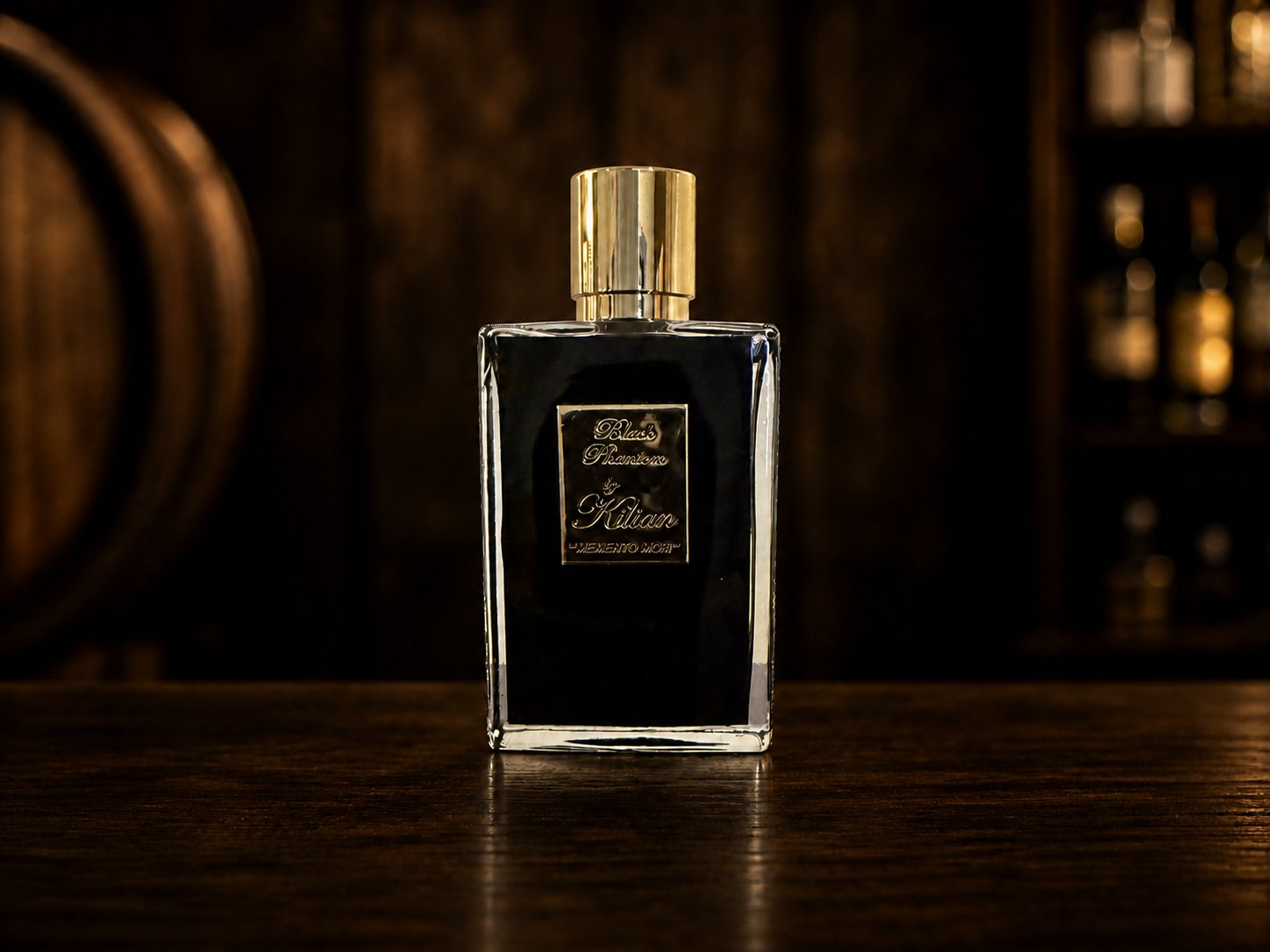 Kilian Black Phantom perfume bottle on a dark bar top with an oak barrel and back-bar shelf softly out of focus behind it