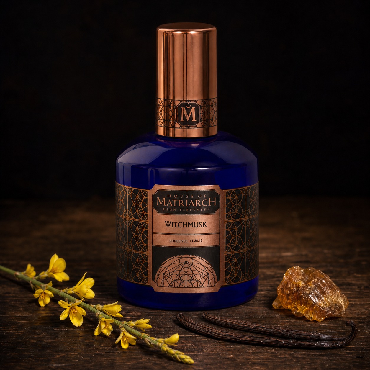 House of Matriarch WitchMusk perfume bottle beside broom flowers, a vanilla pod, and amber resin