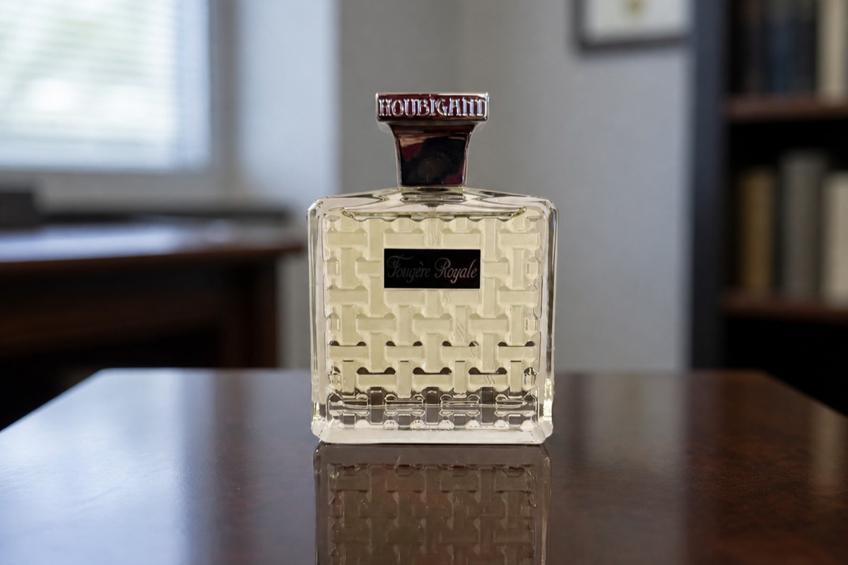 Houbigant Fougère Royale bottle on a dark wood table, a small office interior blurred behind it with window light and a bookshelf