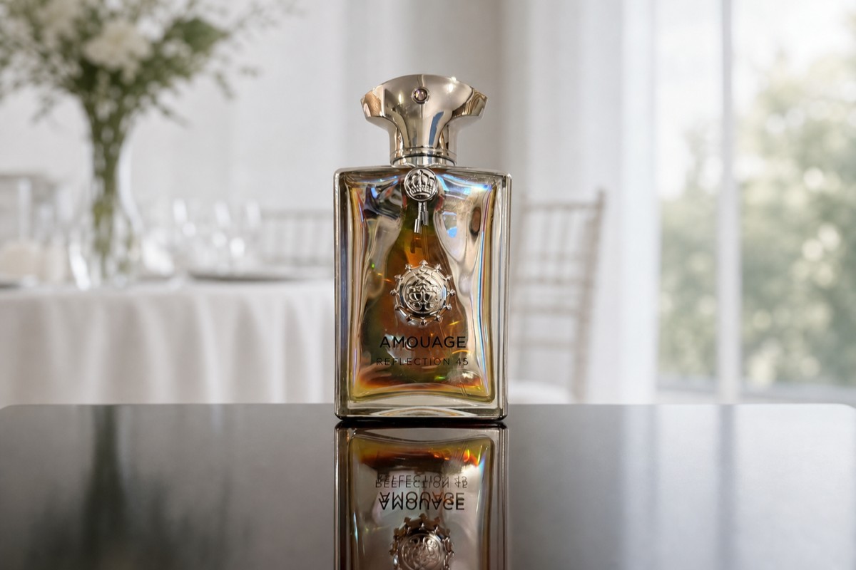 Amouage Reflection 45 bottle on a table, a bright modern wedding reception blurred behind it with white florals and daylight