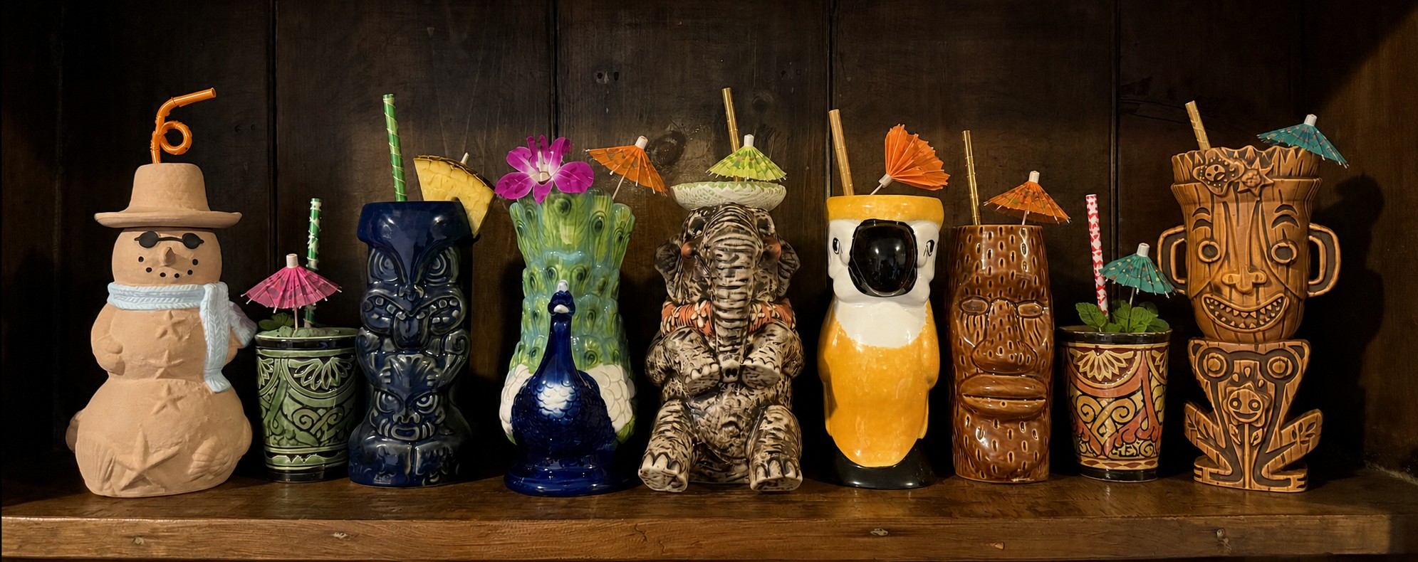 A shelf of tiki mugs, ceramic gods, animals, and a snowman, garnished with straws and cocktail umbrellas